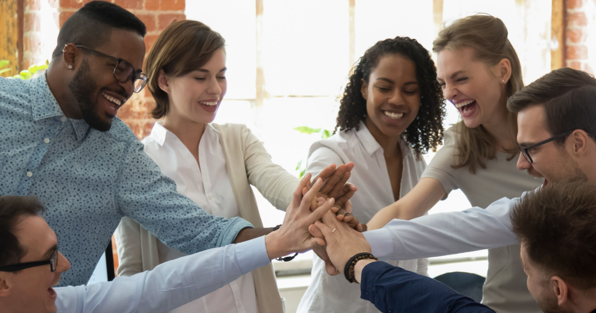 6 Reasons Why Employer Branding Is Fundamental to Marketing in 2023 Various employees happily put their hands together in a cheer representing their contentment in the workplace and how this results in great employer branding.
